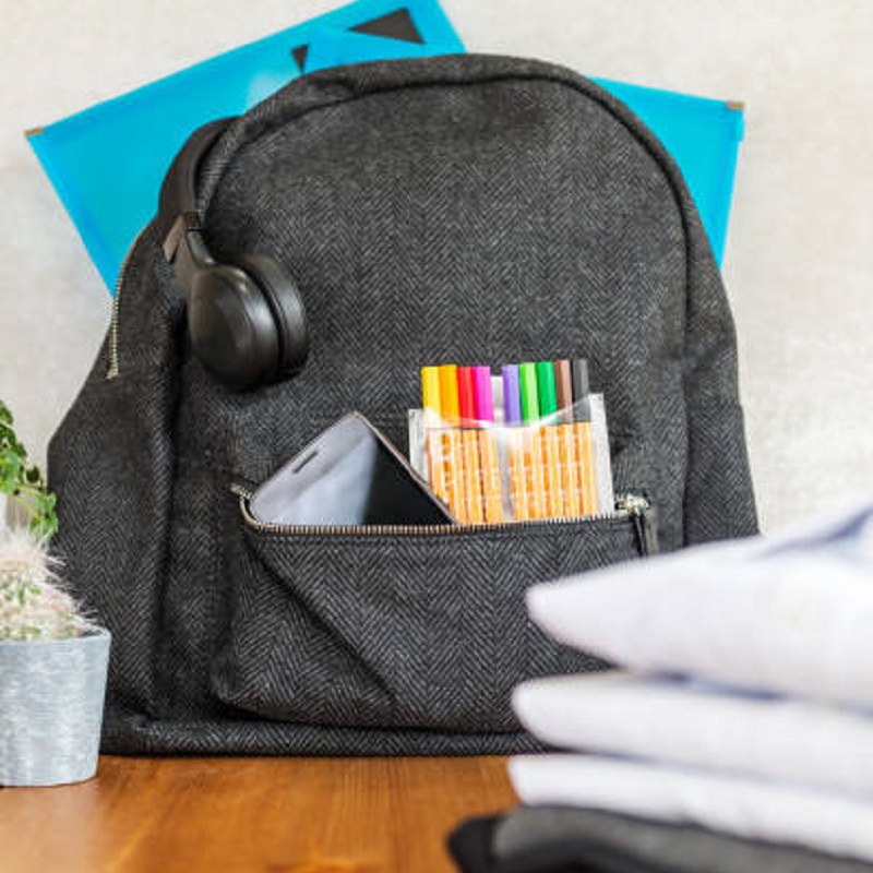 Back to school concept, backpack with school uniform such as white shirts and sweater, as well as electronic devices such as smart watch, mobile phone and headphones on the light background